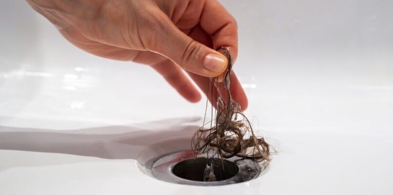 Person using drain snake to remove hair clog from walk-in shower drain