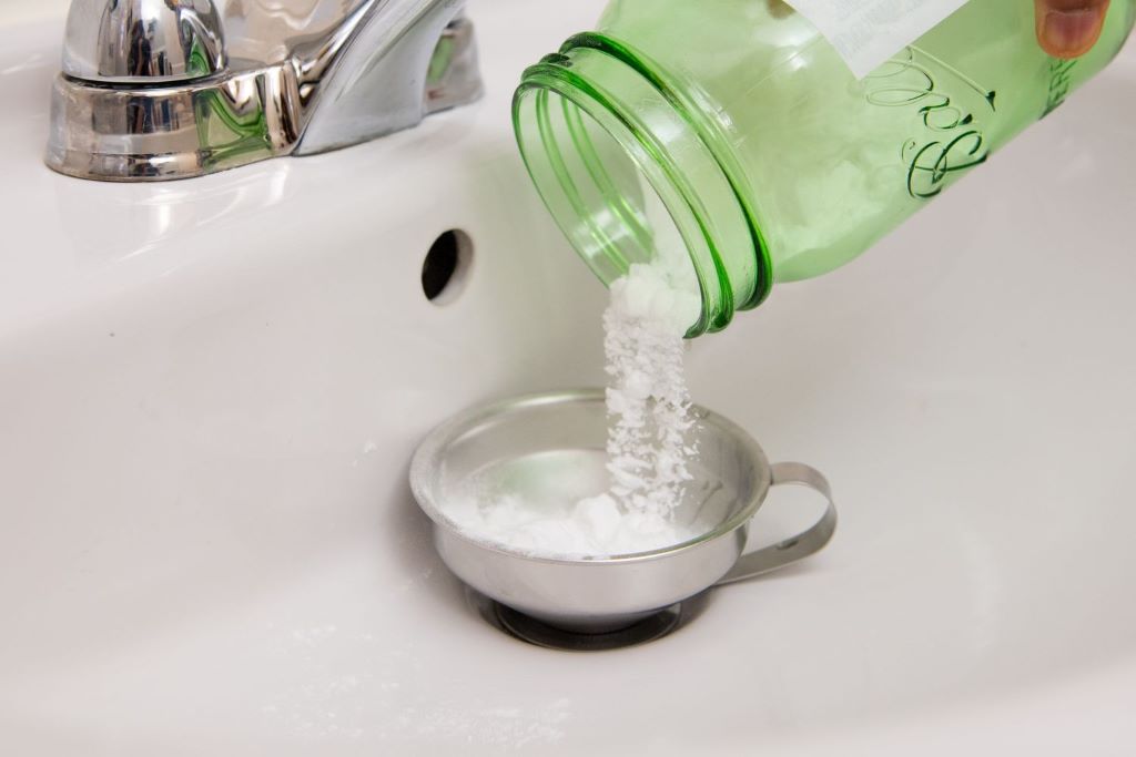 Natural cleaning supplies including baking soda and vinegar for shower drain maintenance