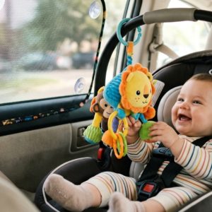 A baby looking at a plush toy next to a car window mesh sunshade.