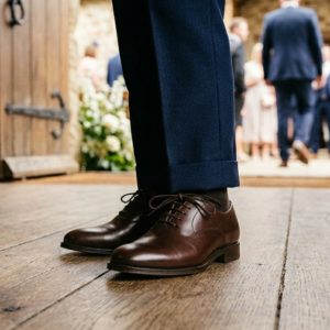 Young boy wearing black velvet formal loafers walks down grassy wedding aisle.